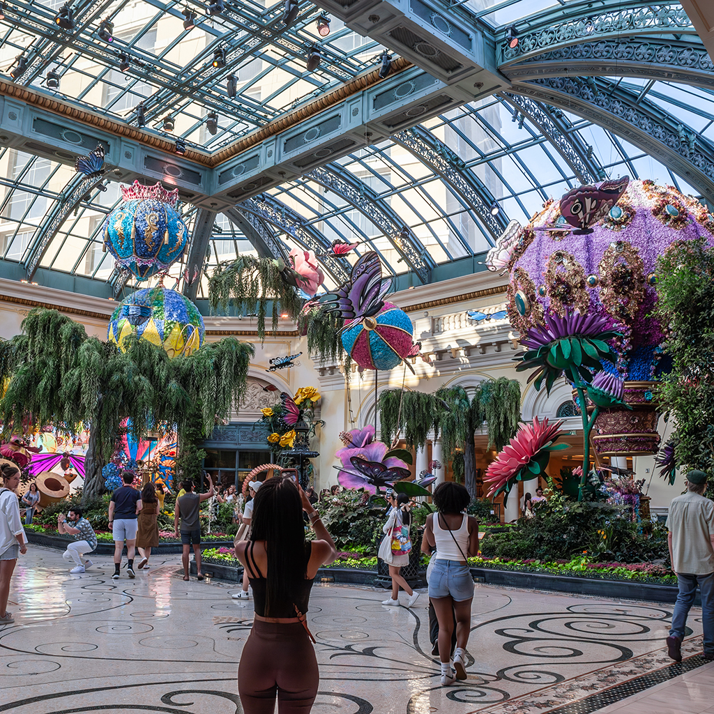Visitors explore the Bellagio Conservatory & Botanical Gardens, admiring floral sculptures under a grand glass ceiling. It's part of Bellagio Hotel & Casino in Las Vegas.